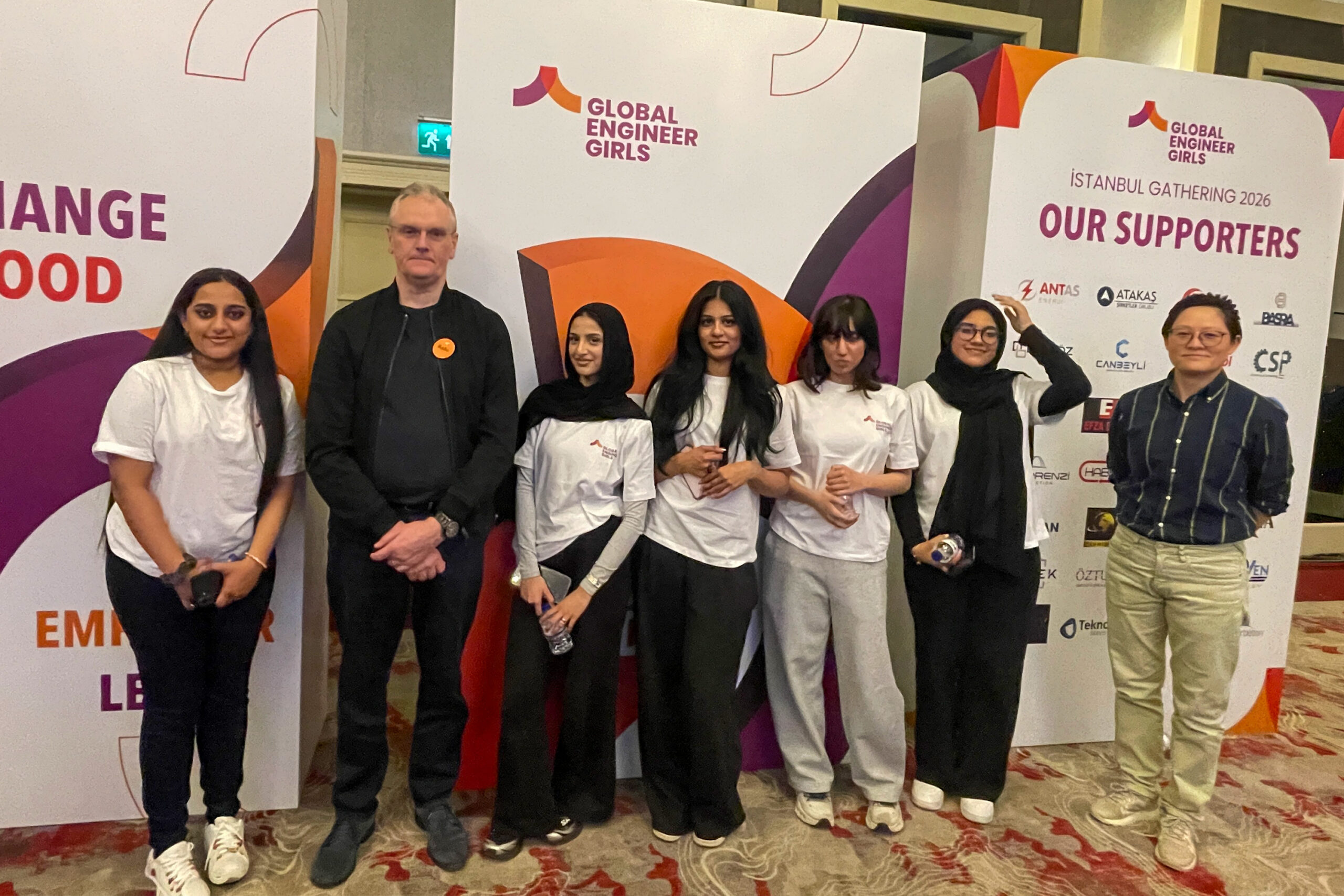 Small group standing beside Global Engineer Girls display boards at Istanbul Gathering 2026, with event branding and supporter logos visible.